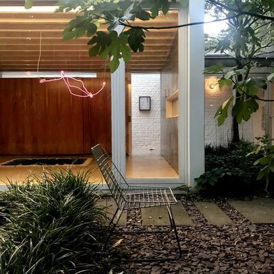 Zicht op de tuinkamer van galerie ZEIT met het voor die ruimte gecreëerde neonwerk Embrace en tegen de bakstenen muur achteraan Beuk, beide van Filip Collin