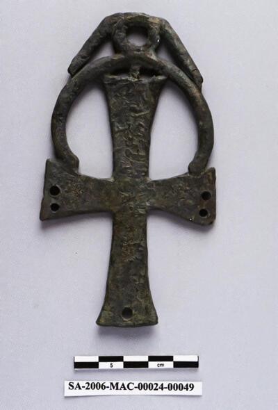 Dit kruis was wellicht een onderdeel van een bronzen kandelaar. In het oog pasten een haak en ketting om het kruis aan de kandelaar te bevestigen. In de gaten in de armen pasten andere haakjes en kettingen, waaraan glazen olielampen werden opgehangen. Sagalassos,