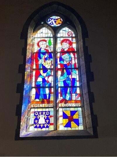 Sint Genesius-Sint-Dionysius afgebeeld in een glasraam van de kerk